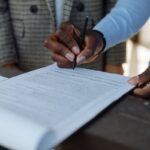 Signature d'un document par une personne noire, un autre individu en costume à proximité