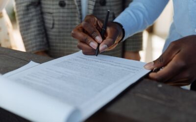 Signature d'un document par une personne noire, un autre individu en costume à proximité