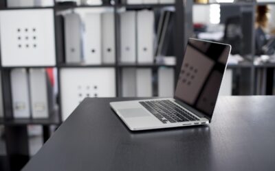Un ordinateur portable sur un bureau avec des classeurs derrière