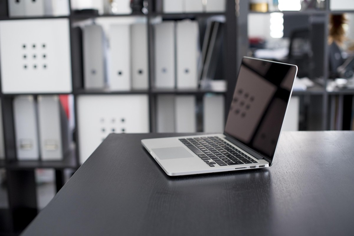 Un ordinateur portable sur un bureau avec des classeurs derrière