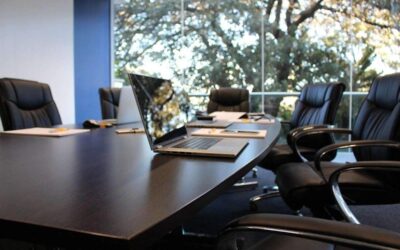 Salle de réunion avec table, ordinateurs, chaises, et vue sur les arbres à travers les fenêtres