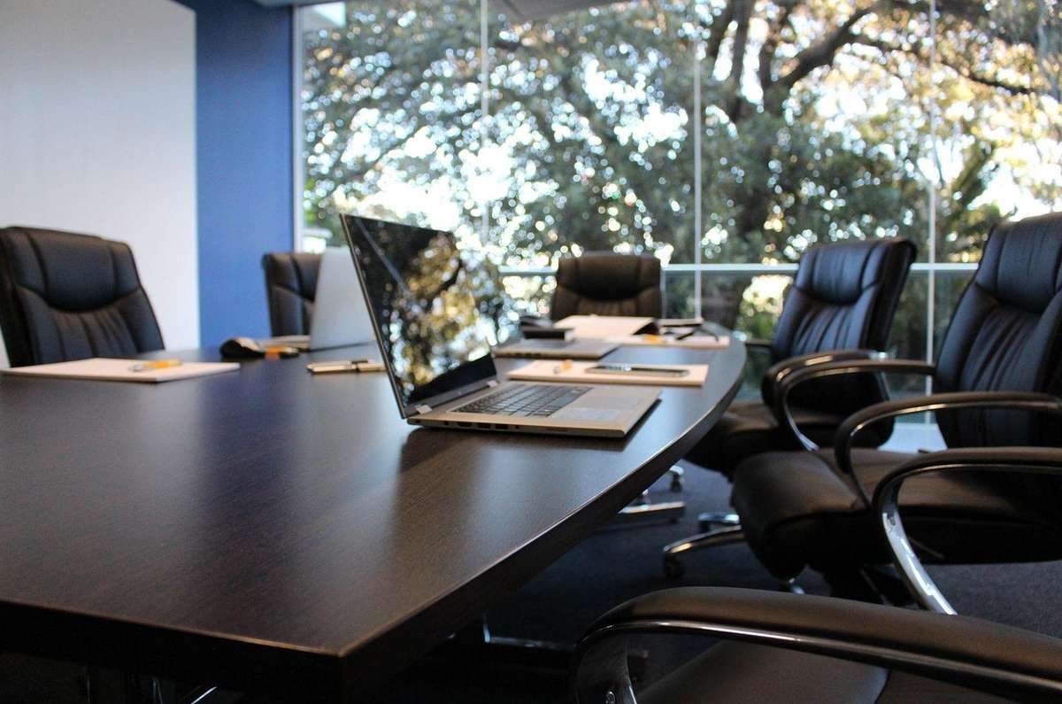 Salle de réunion avec table, ordinateurs, chaises, et vue sur les arbres à travers les fenêtres