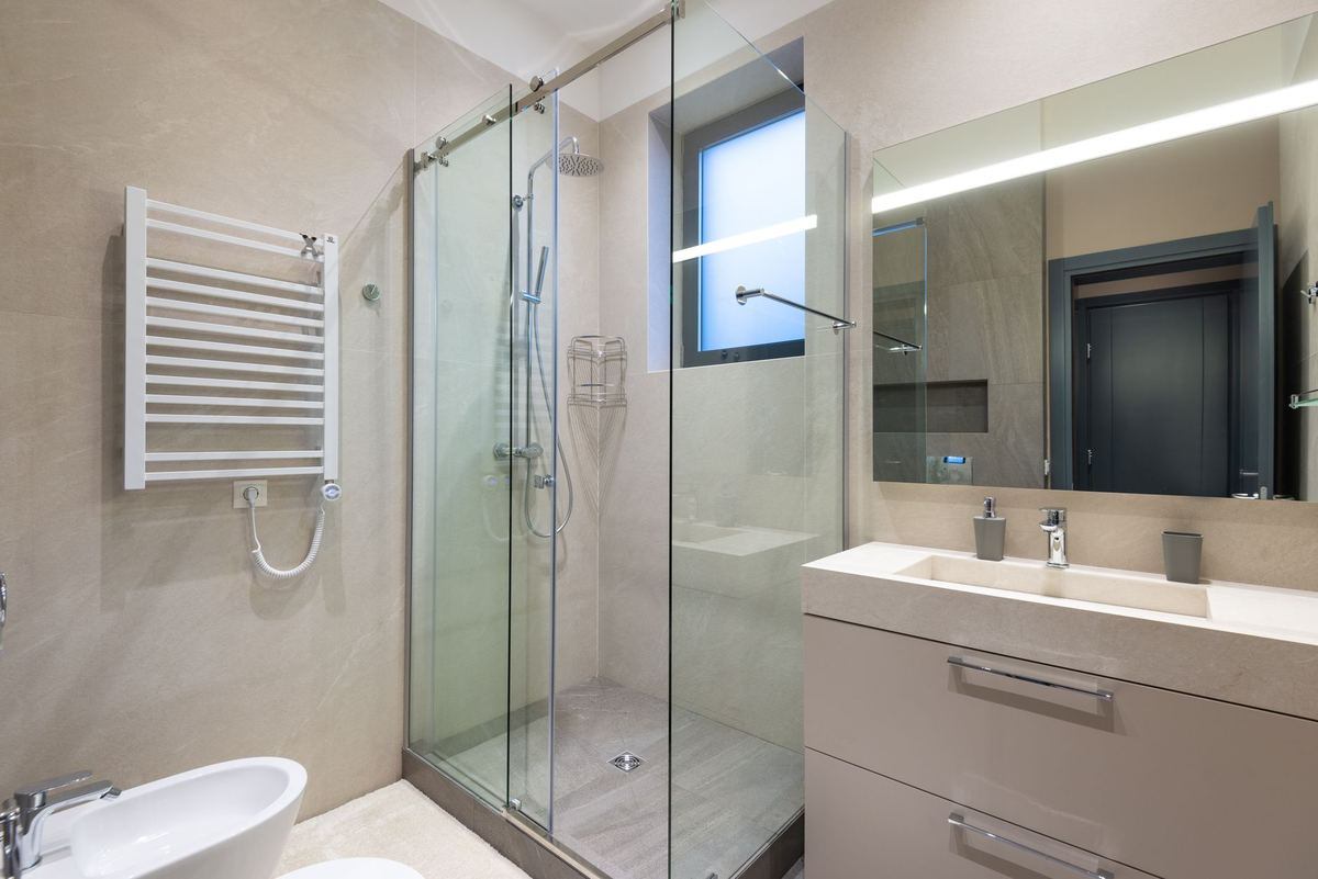 Vue d'une salle de bain moderne avec douche vitrée, vasque et miroir lumineux Vue d'une salle de bain moderne avec douche vitrée, vasque et miroir lumineux