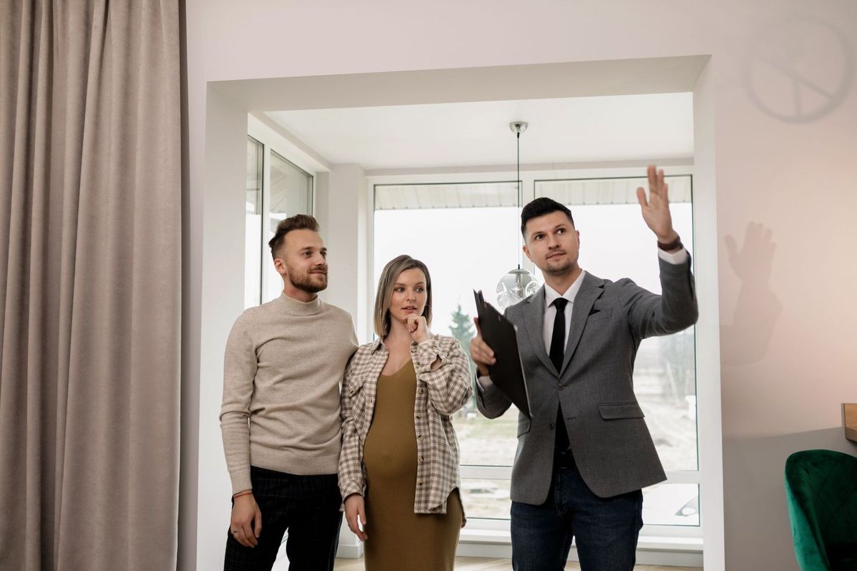 Homme en costume levant la main, femme et homme à côté, intérieur d'une maison
