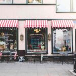 Boutique avec auvents rouges et blancs, vitrines, tables et chaises sur le trottoir