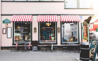 Boutique avec auvents rouges et blancs, vitrines, tables et chaises sur le trottoir