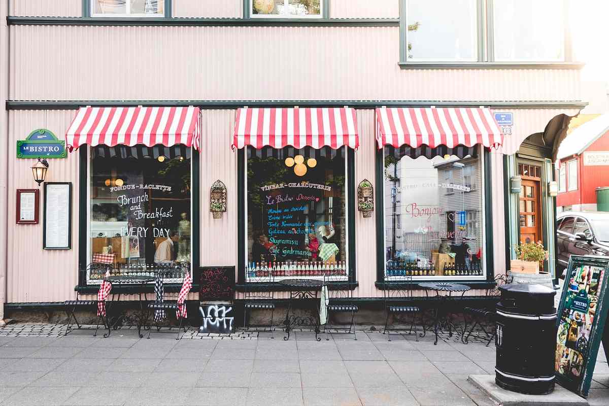 Boutique avec auvents rouges et blancs, vitrines, tables et chaises sur le trottoir