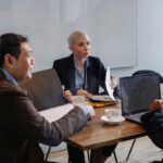 Trois personnes discutent autour d'une table avec ordinateurs et documents